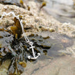 Silver necklace with an anchor pendant on a rock with seaweed on a cornish beach