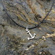 Silver anchor pendant on a black cord against a rocky background