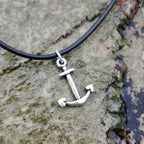 Silver anchor pendant on a black cord against a stony rockpool background