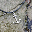 Silver anchor pendant on a black cord against a stony rockpool background