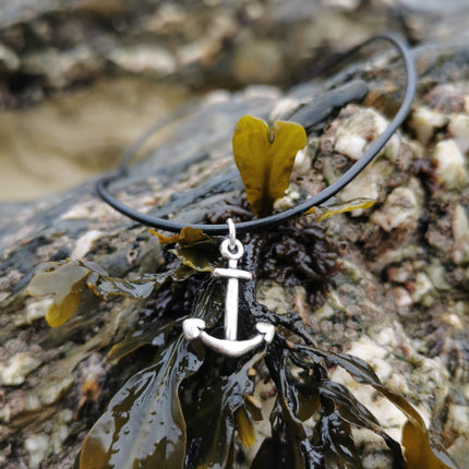 Necklace with an anchor pendant on a background of seaweed and rocks