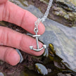 Silver anchor necklace held by a hand over a rockpool in falmouth, cornwall