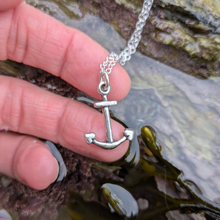Silver anchor necklace held by a hand over a rockpool in falmouth, cornwall