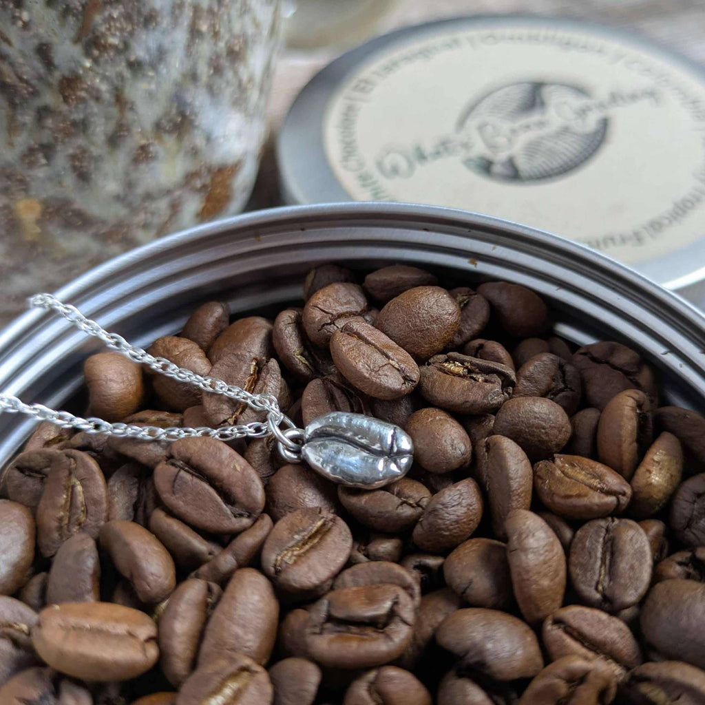 Silver coffee bean charm necklace on coffee beans in a tin
