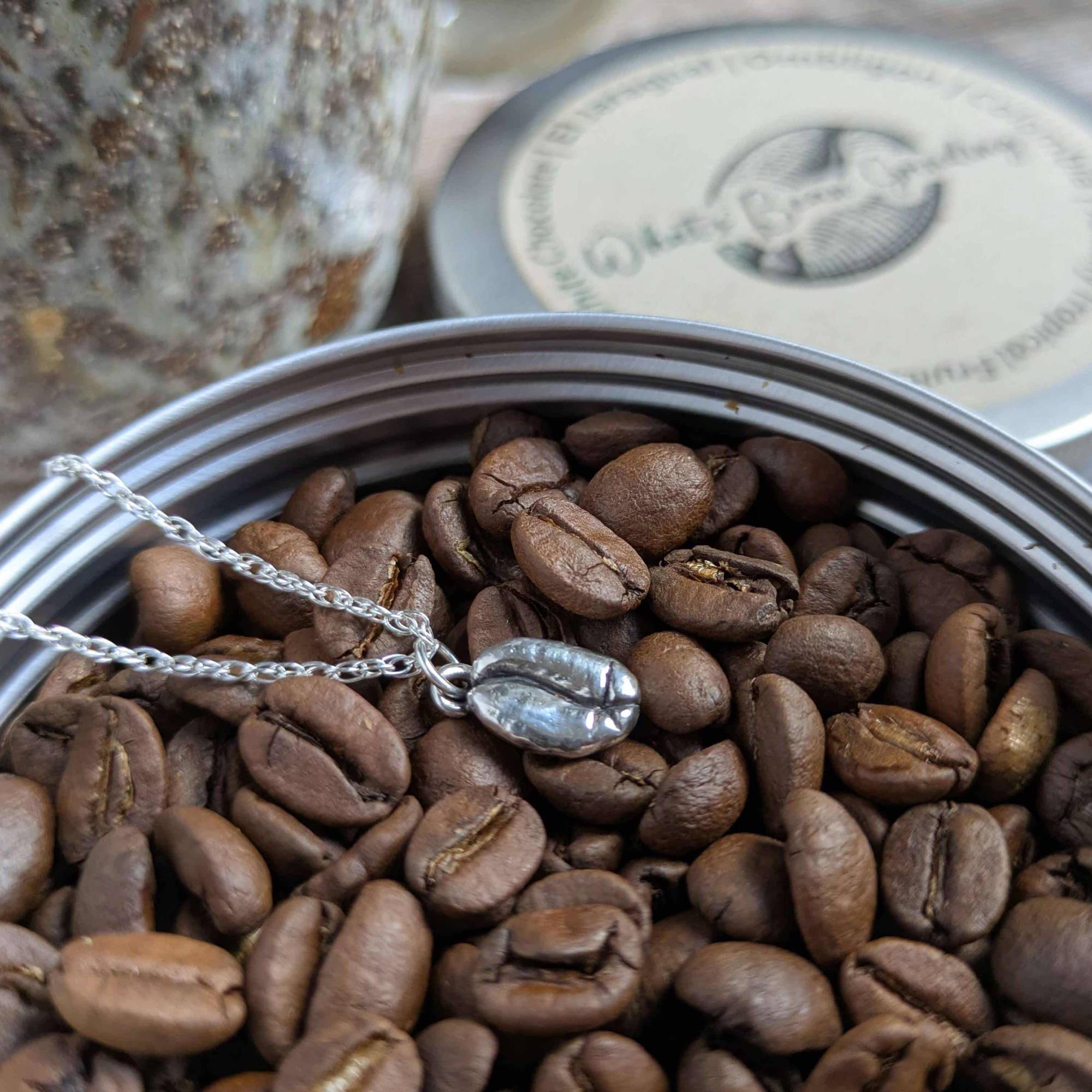 Silver coffee bean charm necklace on coffee beans in a tin