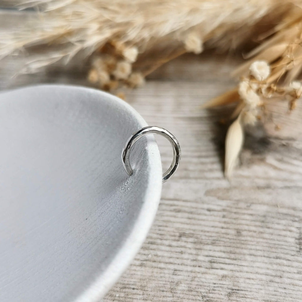 Close-up of a hammered silver ear cuff on a textured surface with dried plants in the background