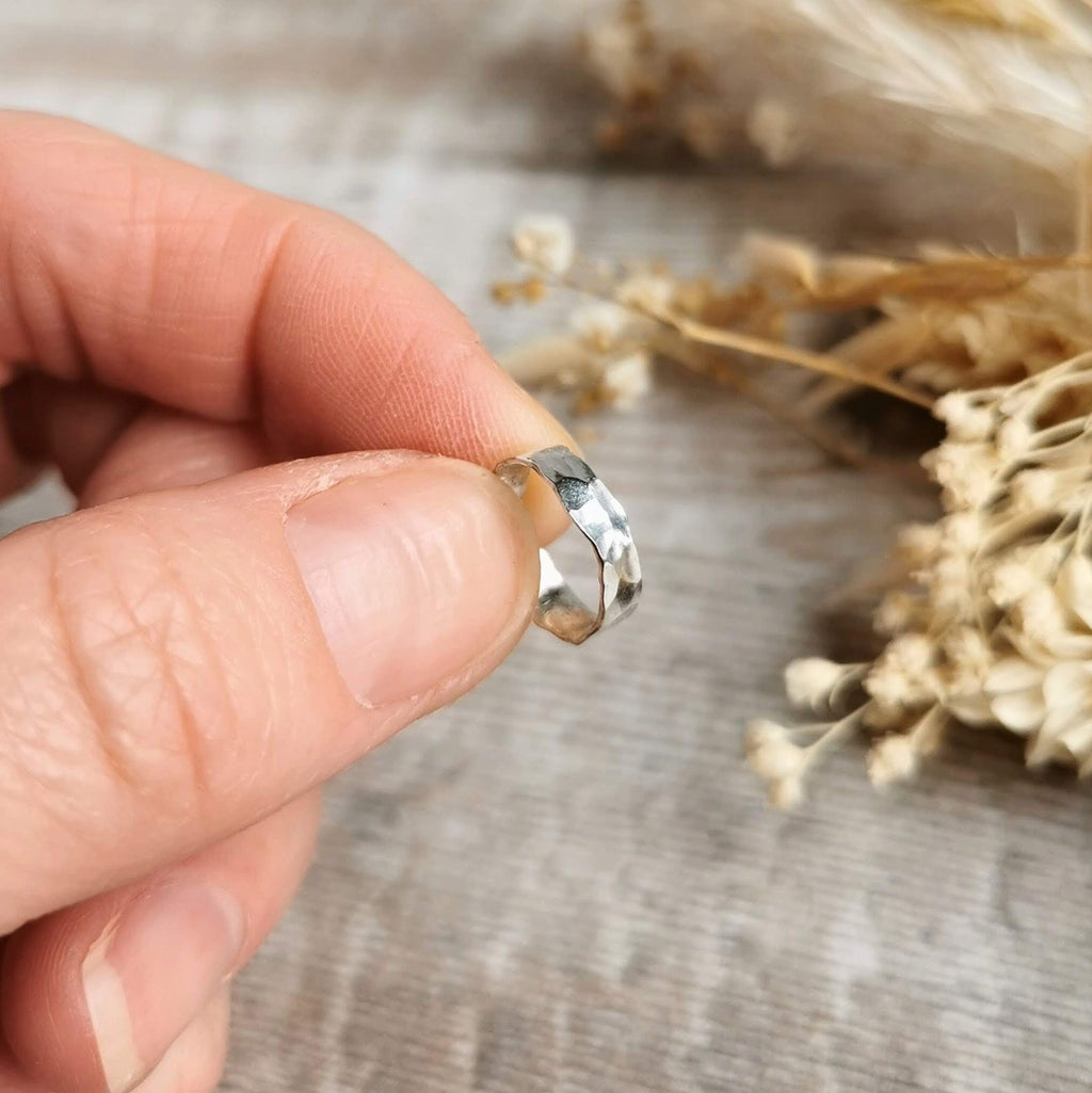 Hand holding a wide hammered silver ear cuff with dried flowers in the background