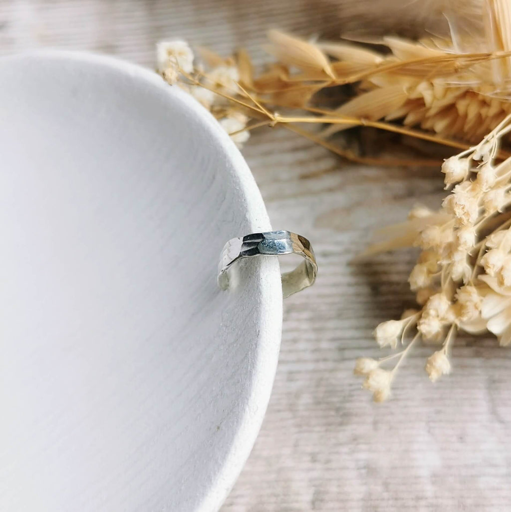 wide silver ear cuff with a hammered texture on a white ceramic plate with dried flowers in the background