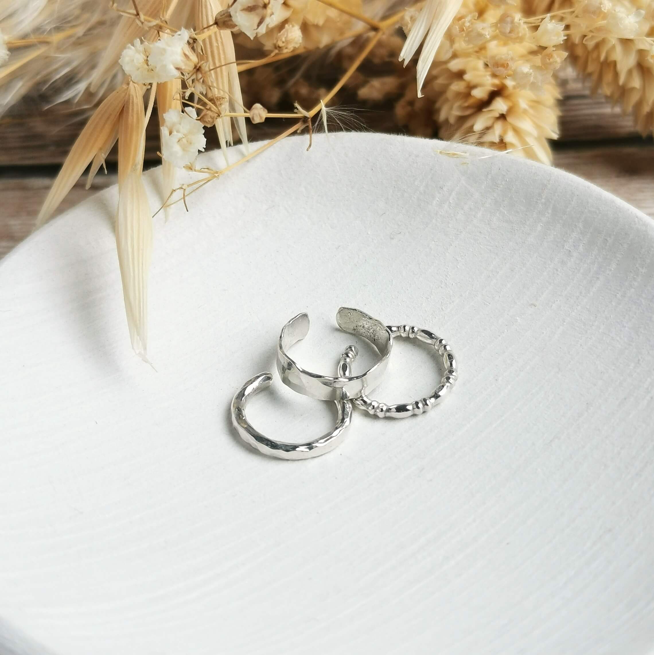 three different textured Silver ear cuffs on a white surface with dried plants in the background