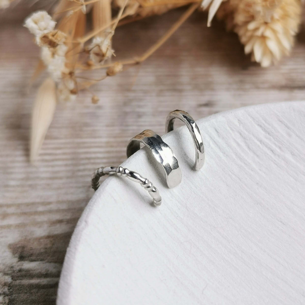Three different styled silver ear cuffs on a white dish with dried flowers in the background