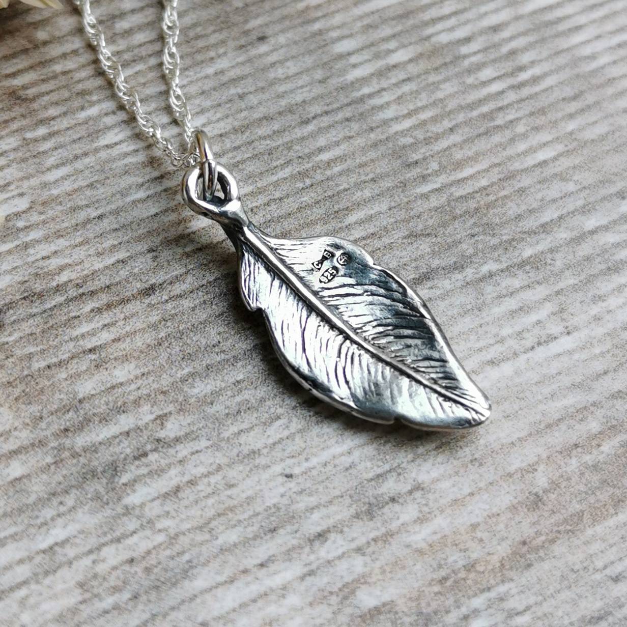 the reverse of a silver feather pendant showing the detail including the hallmark with artist makers mark, sterling silver authentication and assay office mark for Birmingham UK