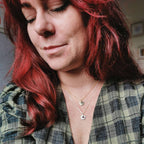 Woman with red hair wearing a plaid shirt and layered mixed metal handmade birthstone necklaces in silver and gold with ruby, turquoise, sapphire and topaz gemstones for july, december, september and october birth months