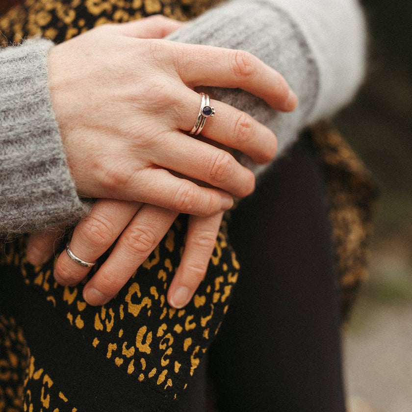 Close-up of hands with silver stacking rings, one with a gemstone and the other two hammered silver, one a midi ring.