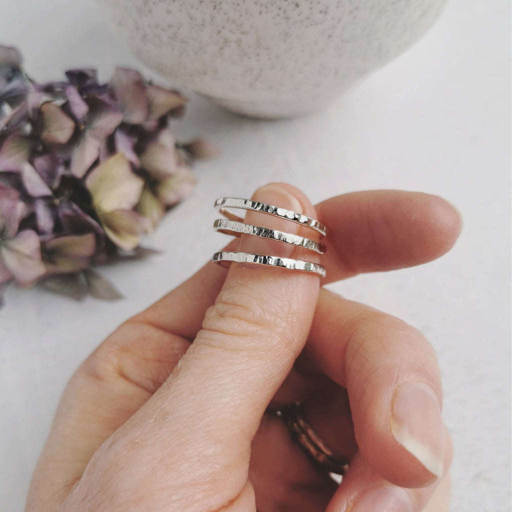 Hand holding three handmade and textured silver rings with a blurred background