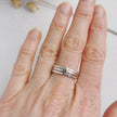 Hand wearing three silver rings on a light background