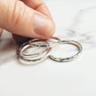 Four silver rings on a marble surface with a hand holding one of them.