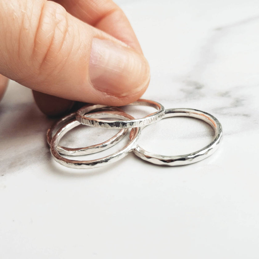 Four silver rings on a marble surface with a hand holding one of them.