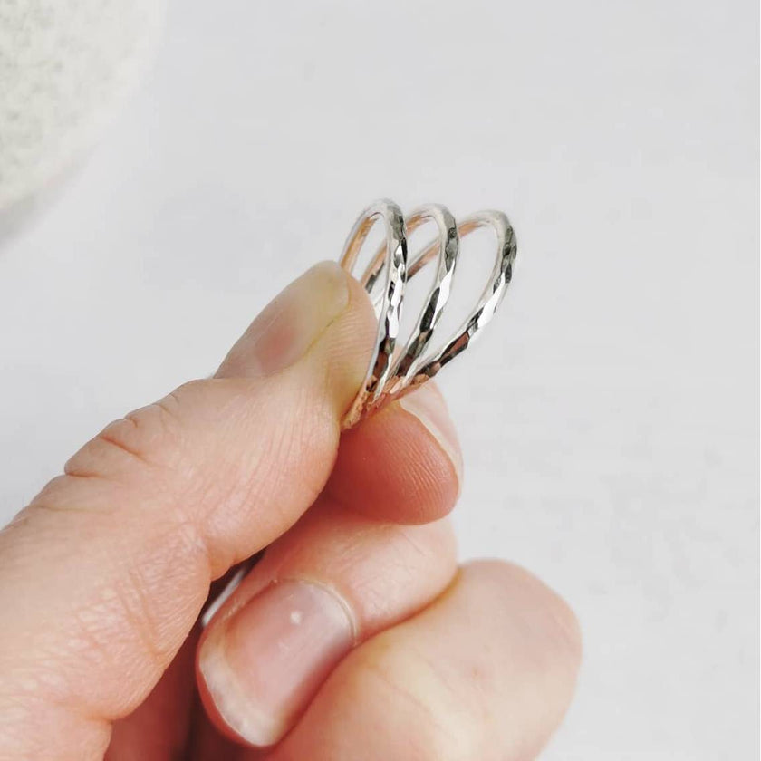 Hand holding three textured silver rings against a light background