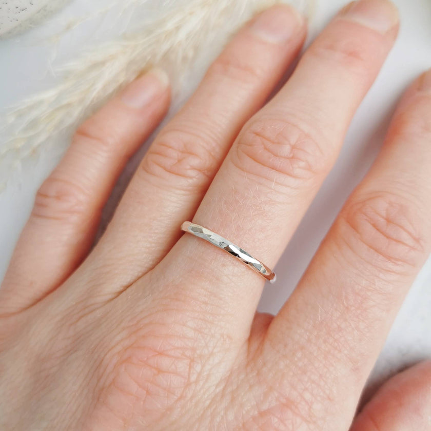 Minimal handmade textured silver ring worn on a finger with a soft background