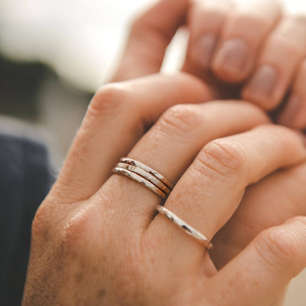 Close-up of a hand wearing textured silver rings with a blurred background