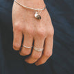 Hand wearing a solid silver bangle bracelet with charms and silver stacking rings against a navy linen dress