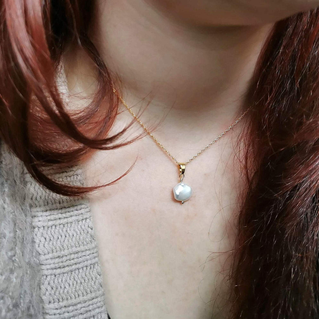 Close-up of a person wearing a gold necklace with a pearl pendant.