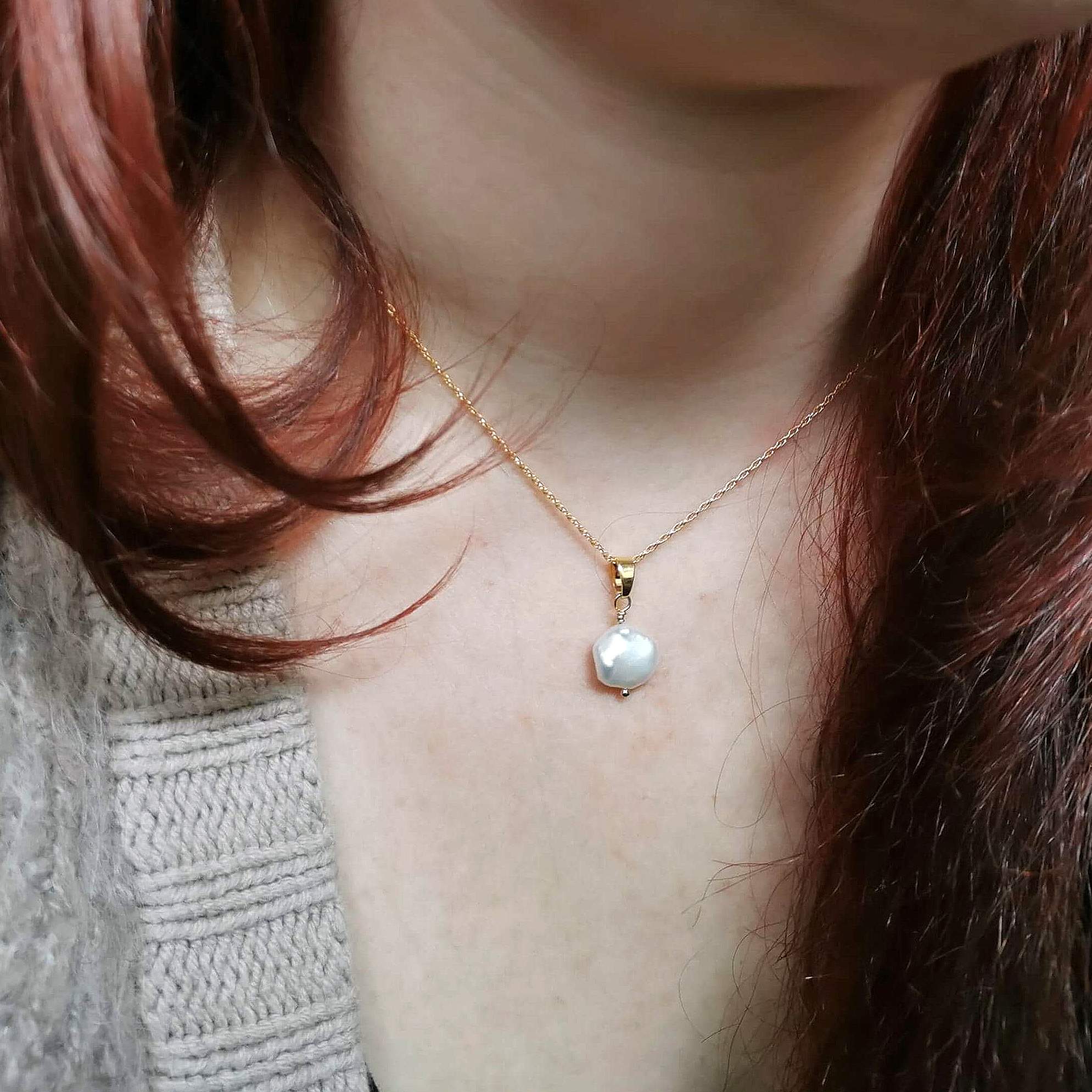 Close-up of a person wearing a gold necklace with a pearl pendant.