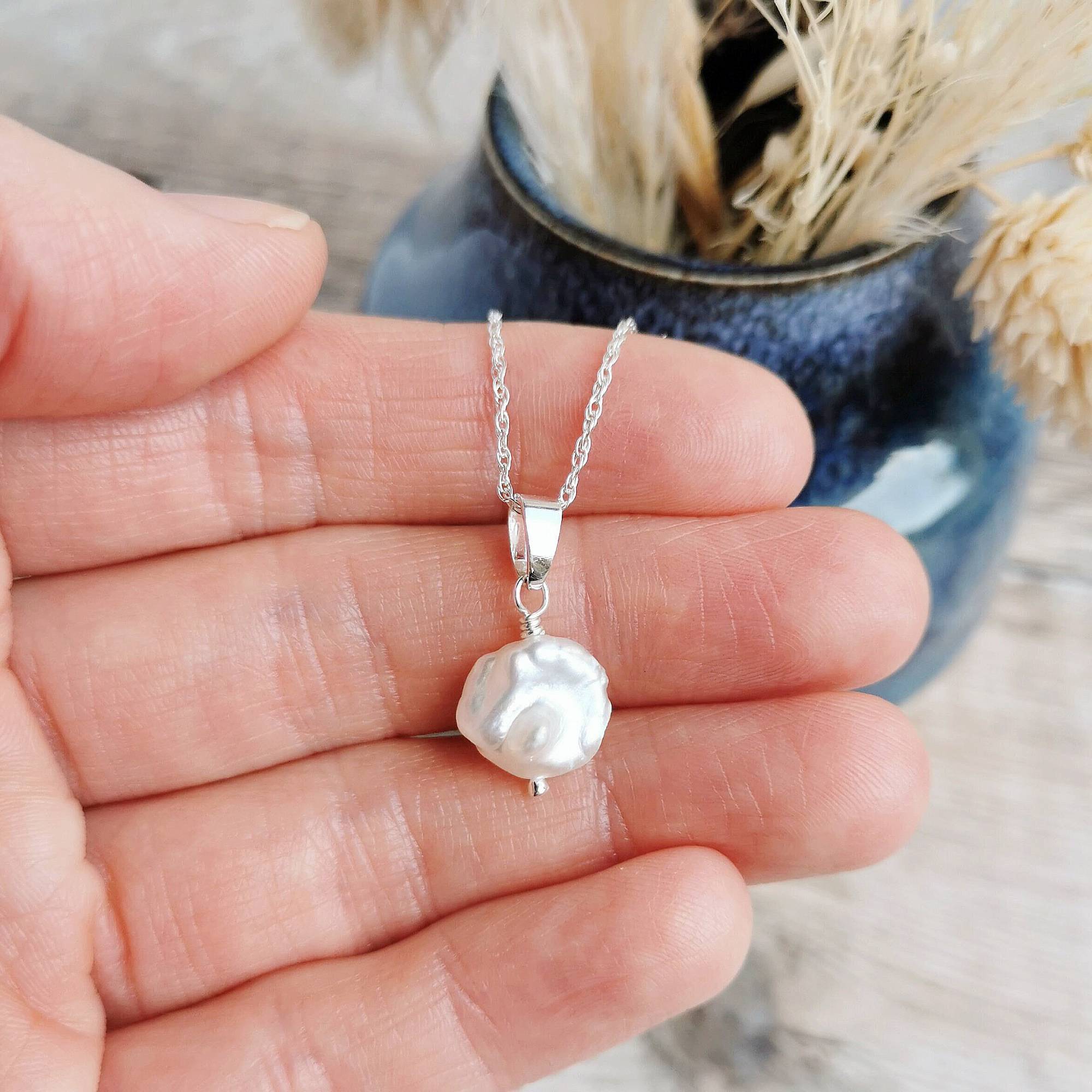 Pearl and silver necklace held in a hand with a blurred natural background