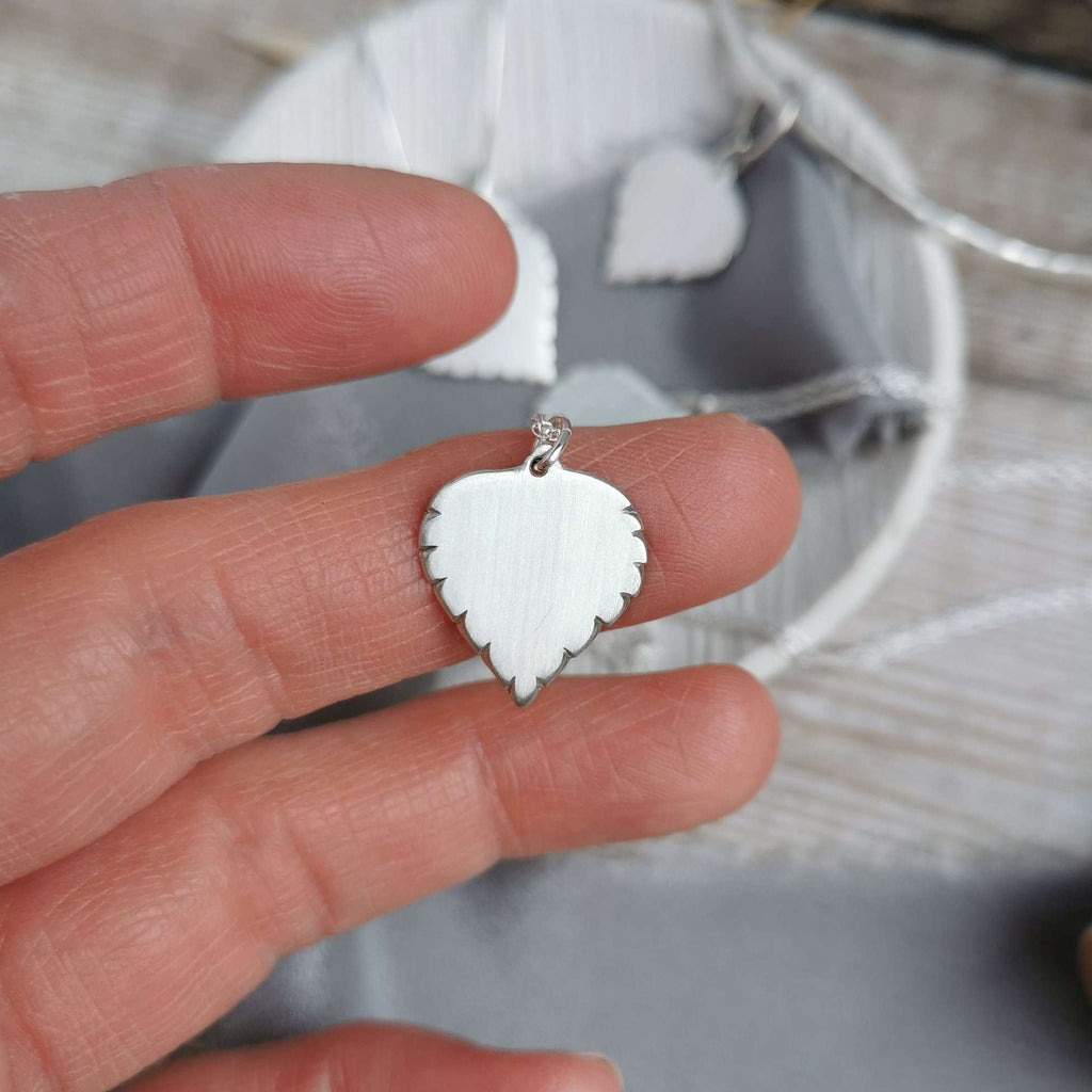 Handmade Silver Birch leaf-shaped pendant held between fingers with a blurred background