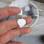 Handmade Silver Birch leaf-shaped pendant held between fingers with a blurred background