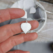 Handmade Silver Birch leaf-shaped pendant held between fingers with a blurred background