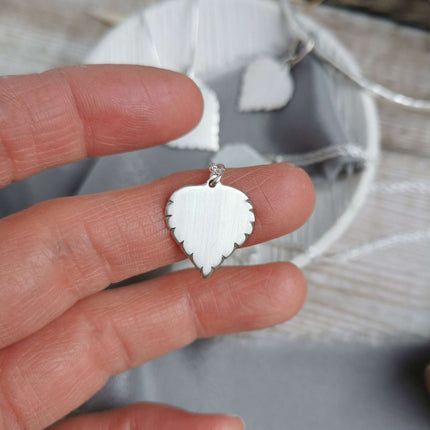 Handmade Silver Birch leaf-shaped pendant held between fingers with a blurred background