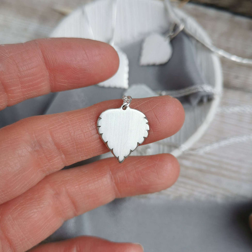 Handmade Silver Birch leaf-shaped pendant held between fingers with a blurred background