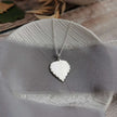 Silver birch leaf-shaped pendant necklace on a grey fabric background