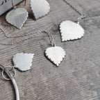 Handmade Silver leaf-shaped jewellery on a textured wooden surface