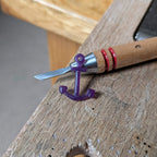 Hand carving tool with a purple anchor-shaped wax sculpture on a work bench