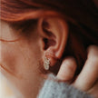 Close-up of an ear wearing a silver mini mantra stud earring with a blurred background