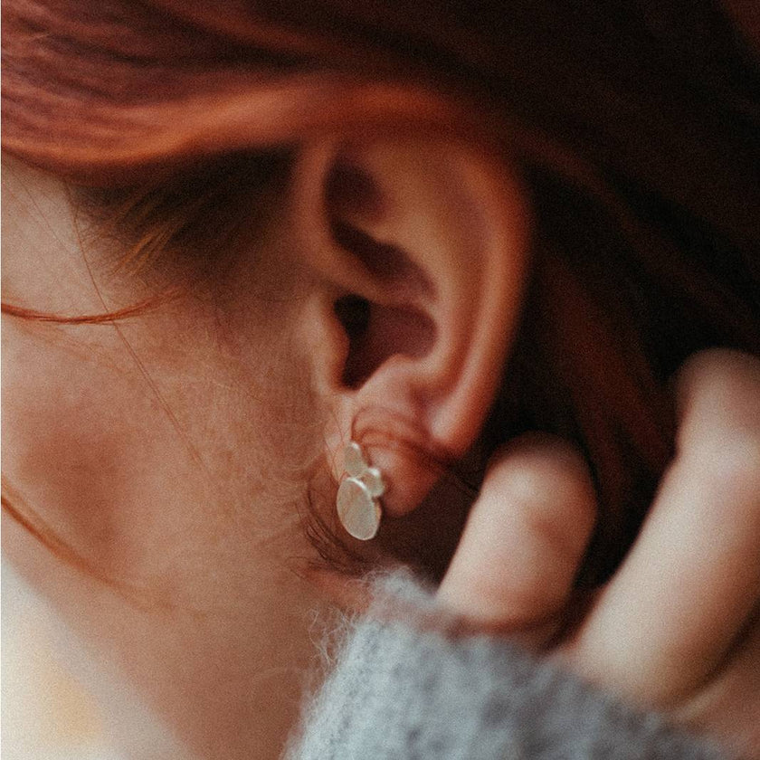 Close-up of an ear wearing a silver mini mantra stud earring with a blurred background